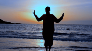 Silhouette of a person with arms raised against a serene, colorful sky at sunrise or sunset, symbolizing a moment of peace, spiritual connection, and openness to growth, reflecting the unity of health and spirituality in Qigong practice.