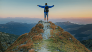 Person standing on a mountain peak with arms outstretched, overlooking a vast landscape at sunrise, symbolizing freedom, achievement, and reflection. The scene captures 'The Modern Journey of Healing & Awakening,' representing personal growth, resilience, and connection to nature.