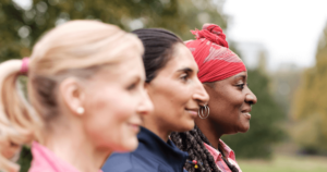 A diverse group of three women stand in profile, facing forward with calm and focused expressions, symbolizing strength and unity. Each woman, from different backgrounds and ages, brings a sense of individuality and shared purpose. Set outdoors, this image captures the essence of conscious aging, resilience, and the journey of embracing one's golden years through mindful practices like Qigong.