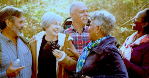 A cheerful group of older adults enjoying a day outdoors, sharing laughter and companionship. They are dressed warmly, some carrying binoculars and walking sticks, indicating a nature walk or shared adventure. This image embodies the spirit of 'Embrace Your Golden Years,' celebrating vitality, connection, and the joy of conscious aging supported by practices like Qigong for enhanced well-being.