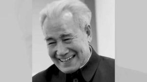 Black and white photograph of Dr. Pang smiling warmly, wearing a traditional Chinese jacket. His expression is joyful, with eyes gently closed in laughter, showing a deep sense of peace and happiness.
