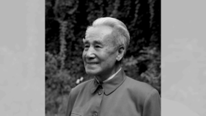Portrait of Dr. Pang, a revered figure in Qigong practice, smiling and looking thoughtfully ahead, set against a natural, leafy backdrop.