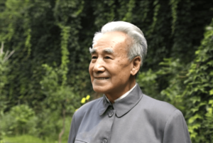 Dr. Pang Ming standing outdoors with a gentle smile, embodying wisdom and serenity, surrounded by greenery, reflecting the spirit of Qigong.