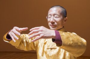 Master Mingtong Gu practicing Qigong with eyes closed, hands gracefully positioned in a meditative posture, embodying energy flow and inner peace
