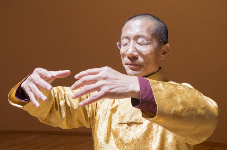 Master Mingtong Gu practicing Qigong with eyes closed, hands gracefully positioned in a meditative posture, embodying energy flow and inner peace