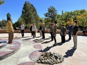 Master Mingtong Gu leading an outdoor Qigong practice with a diverse group of participants, standing attentively under a bright blue sk