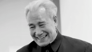 Black and white photograph of Dr. Pang smiling warmly, wearing a traditional Chinese jacket. His expression is joyful, with eyes gently closed in laughter, showing a deep sense of peace and happiness.