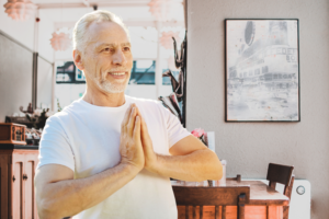 Smiling man practicing Wisdom Healing Qigong with palms together in a prayer-like pose, radiating joy, inner peace, and mindfulness in a serene space