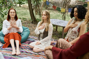 Group of women meditating outdoors with hands on their hearts, focusing on a 7 Weeks of Sound Healing practice, fostering connection and inner peace.