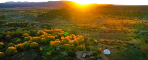 A breathtaking sunset over the Southwest Sanctuary, casting warm golden light over the landscape with vibrant trees and hills, symbolizing peace, healing, and natural beauty.