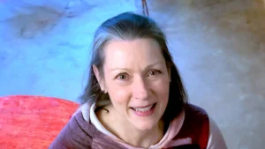 Portrait of Annie Gedye, smiling warmly with a vibrant red chair and soft blue background, creating an inviting and uplifting atmosphere.