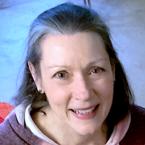 Portrait of Annie Gedye, smiling warmly with a vibrant red chair and soft blue background, creating an inviting and uplifting atmosphere.
