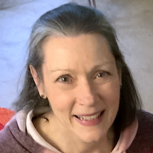 Portrait of Annie Gedye, smiling warmly with a vibrant red chair and soft blue background, creating an inviting and uplifting atmosphere.