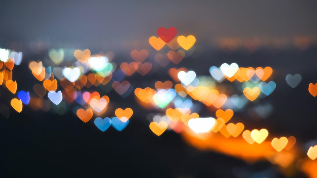 A vibrant night scene with colorful heart-shaped bokeh lights in various hues of orange, red, blue, and white, creating a dreamy and romantic atmosphere