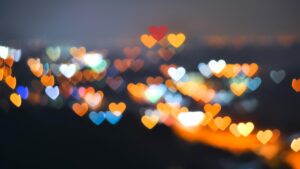 A vibrant night scene with colorful heart-shaped bokeh lights in various hues of orange, red, blue, and white, creating a dreamy and romantic atmosphere