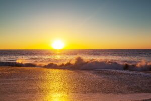 Golden sunset over the ocean with waves crashing onto the shimmering shore, creating a serene and breathtaking seascape—ideal for themes of relaxation, meditation, beach retreats, and coastal travel inspiration.
