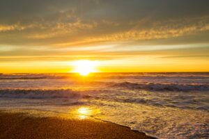Golden sunrise over the ocean with waves gently crashing onto the shore, illuminating the sky and water with warm hues—symbolizing new beginnings, inner peace, and the power of natural renewal.