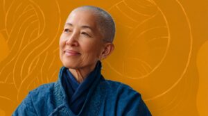 An older woman with a shaved head looks off to the side with a peaceful, confident smile. She wears a textured blue jacket and matching scarf. The background is a warm golden-orange with soft, flowing line illustrations, creating a serene and contemplative atmosphere.